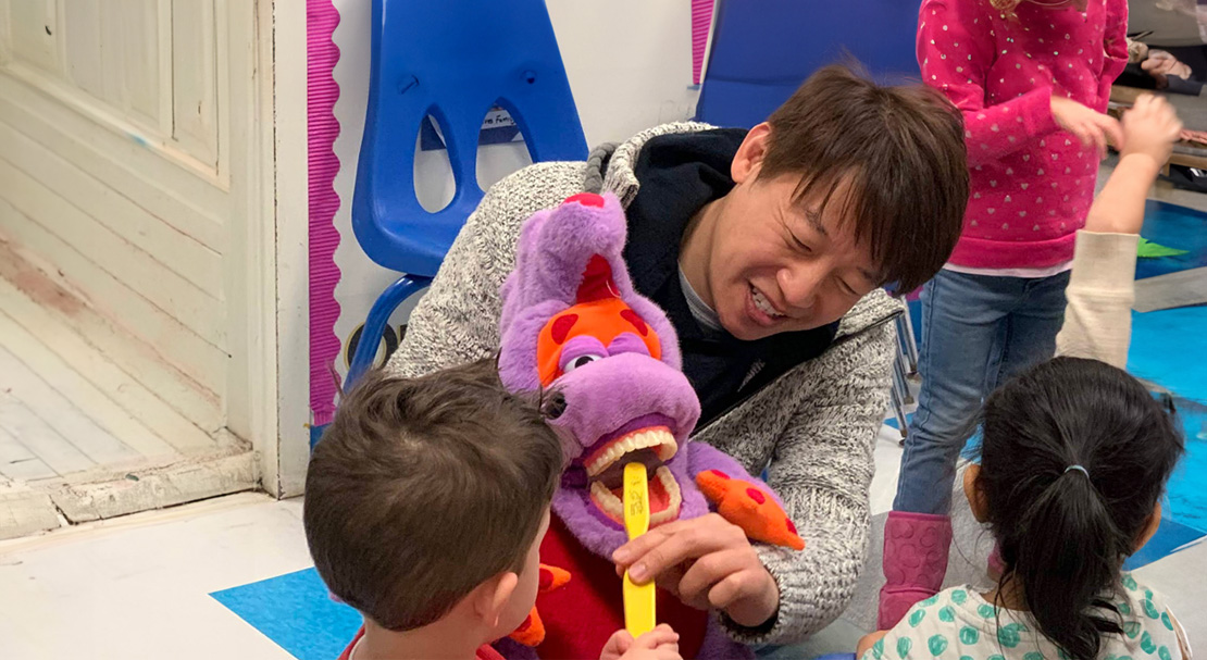 A person holding a child s hand while they interact with a large purple stuffed animal.