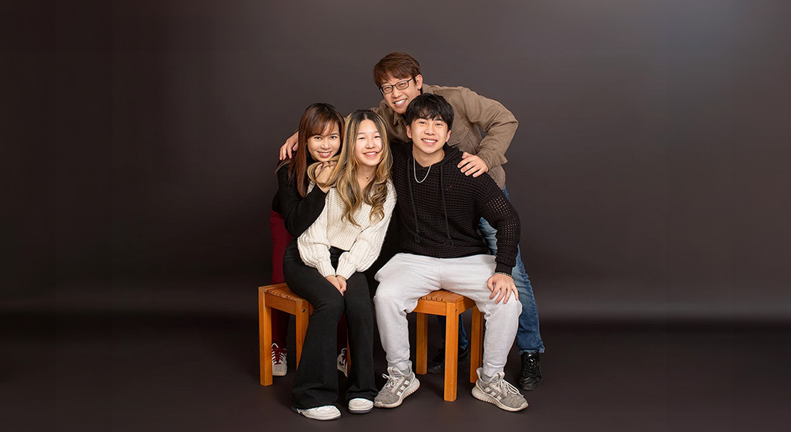 Four individuals posing together with smiles, seated on a bench against a background wall.