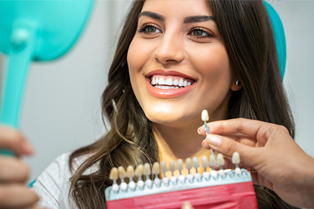 The image depicts a woman with long hair smiling at the camera while holding a red hair clipper, with her hands positioned over a white comb.
