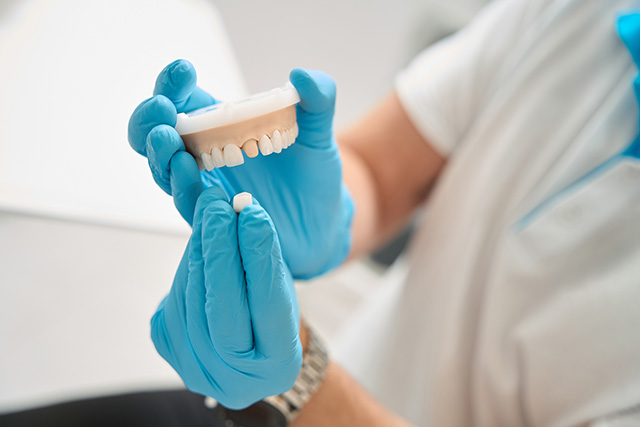A dental professional holding a tooth, wearing gloves and a white coat, with a focus on the tooth and glove in the foreground.