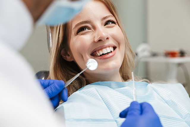 A woman sitting in a dental chair while receiving dental care from a professional wearing protective gear.
