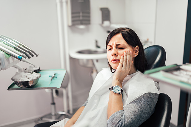 A woman with closed eyes, seated at a dental chair, receiving a dental check-up.