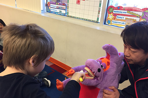 A young child is being assisted by an adult with a purple dinosaur toy.
