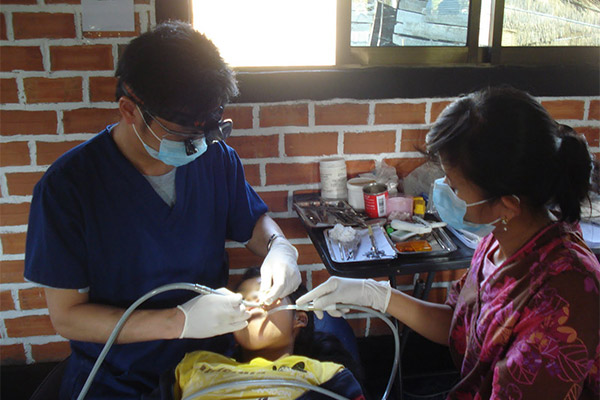 A medical professional performing a procedure on a patient with the assistance of another person, likely in a makeshift surgical setting.