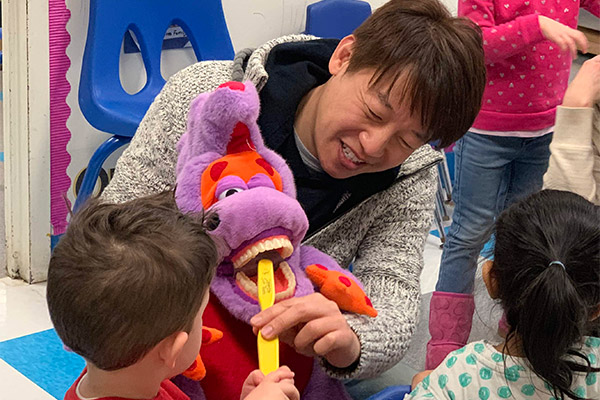 A man holding a large purple dinosaur puppet with children around him, possibly during an event or show.