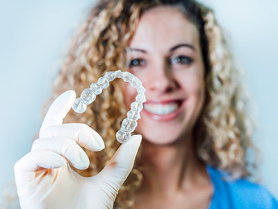 The image shows a person holding up a transparent heart-shaped object resembling a mouthguard or dental appliance, with a smile.