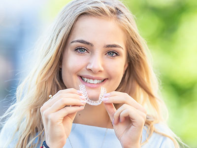 An individual is holding up a toothbrush with a smile while showing off a clear dental appliance.