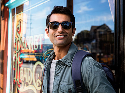A man wearing sunglasses and standing outside a shop, smiling slightly at the camera.