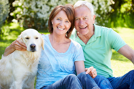An elderly couple sitting outdoors with a large golden retriever dog.